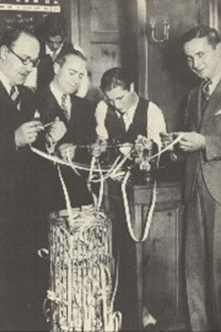 People looking at ticker tape in front of a stock ticker (ca. 1929). Wikimedia Commons. Public Domain